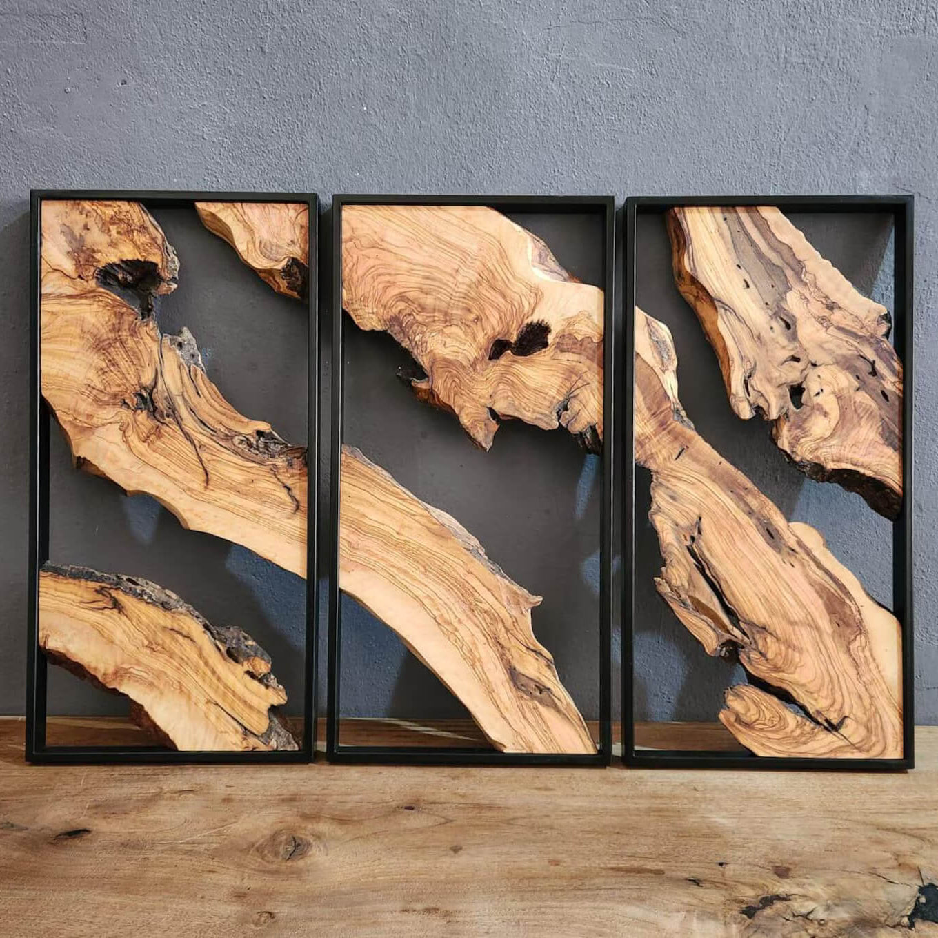 Three framed pieces of wood with natural patterns on a gray wall.